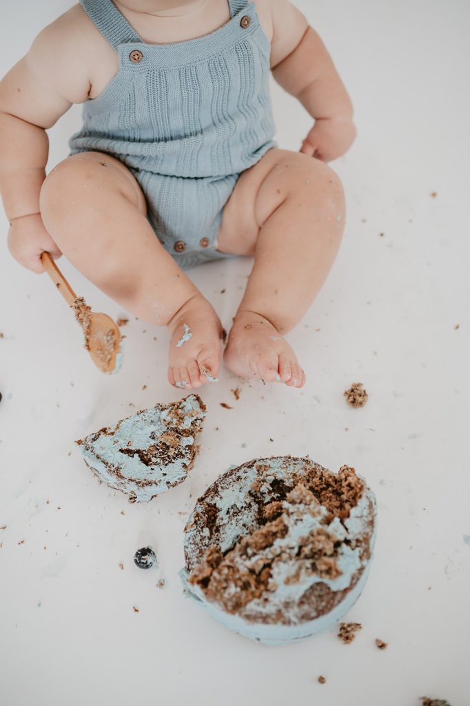cake smashed with wooden spoon by baby wearing blue 
