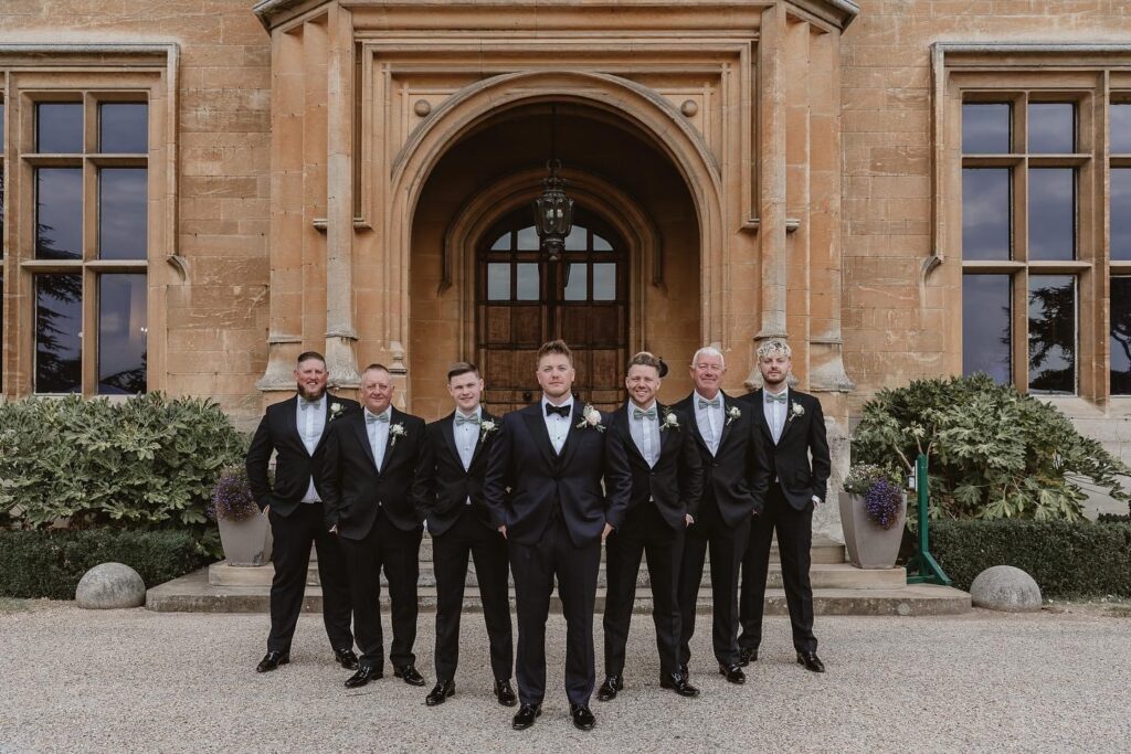 black tie groom with wedding party standing with hands in pockets outside the venue in a arrow form