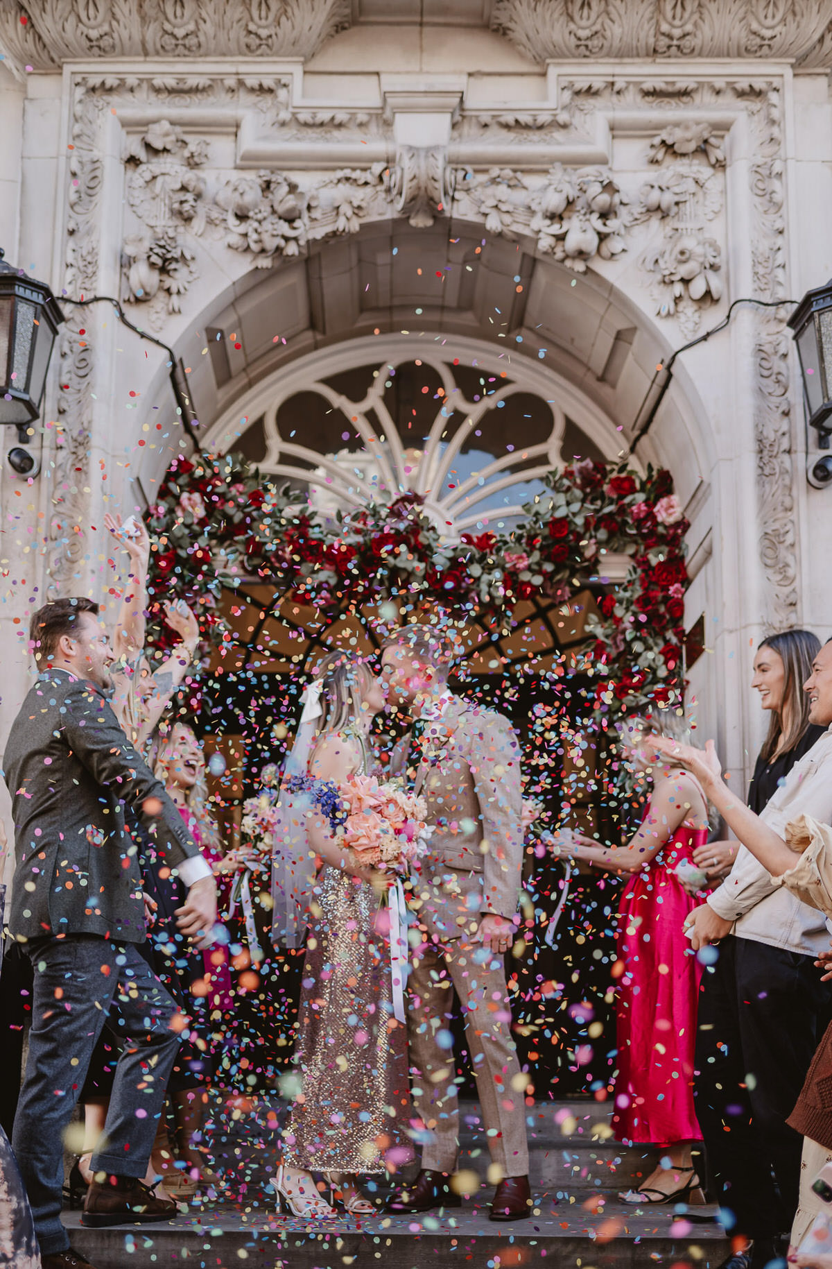 paper confetti being thrown in the air by wedding guests after the ceremony at the venue over the bride and groom while they kiss on the steps