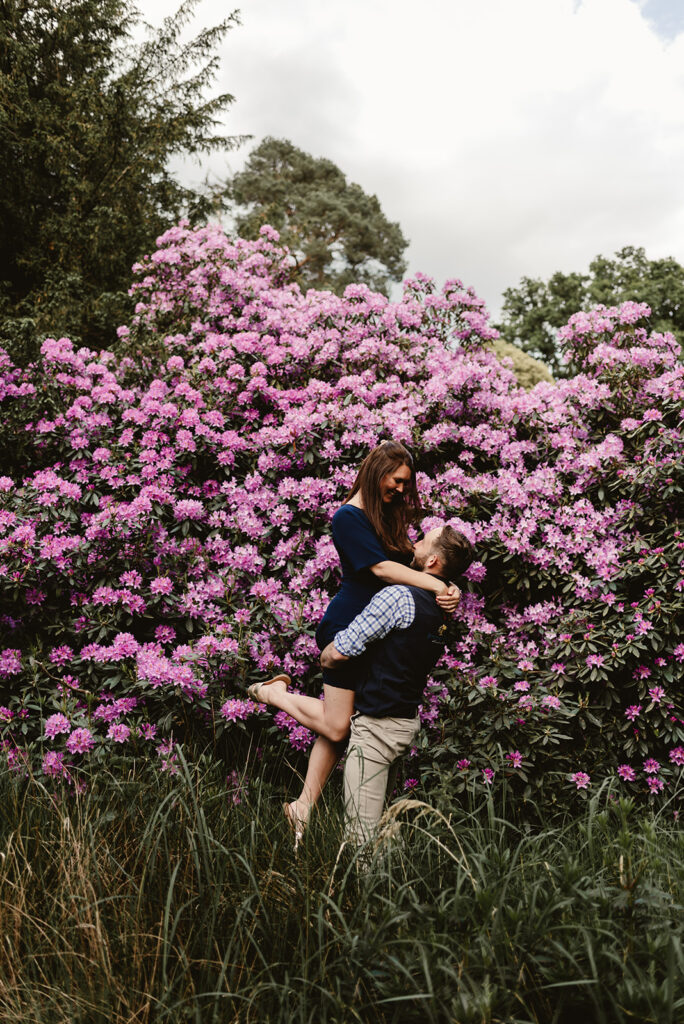 couple do a bum lift and flick of the leg while up in the air while near the purple flowers