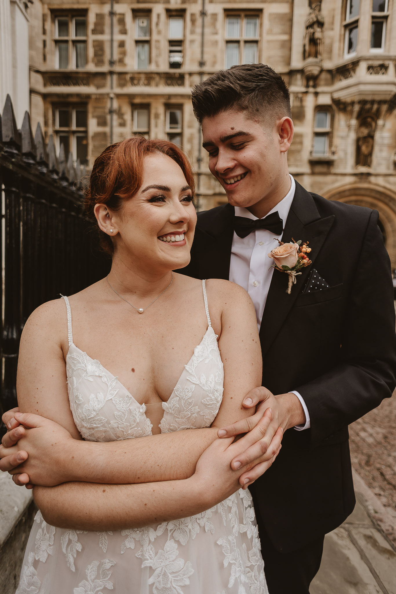 bride standing in front of groom with arms crossed smiling in the middle of Cambridge city