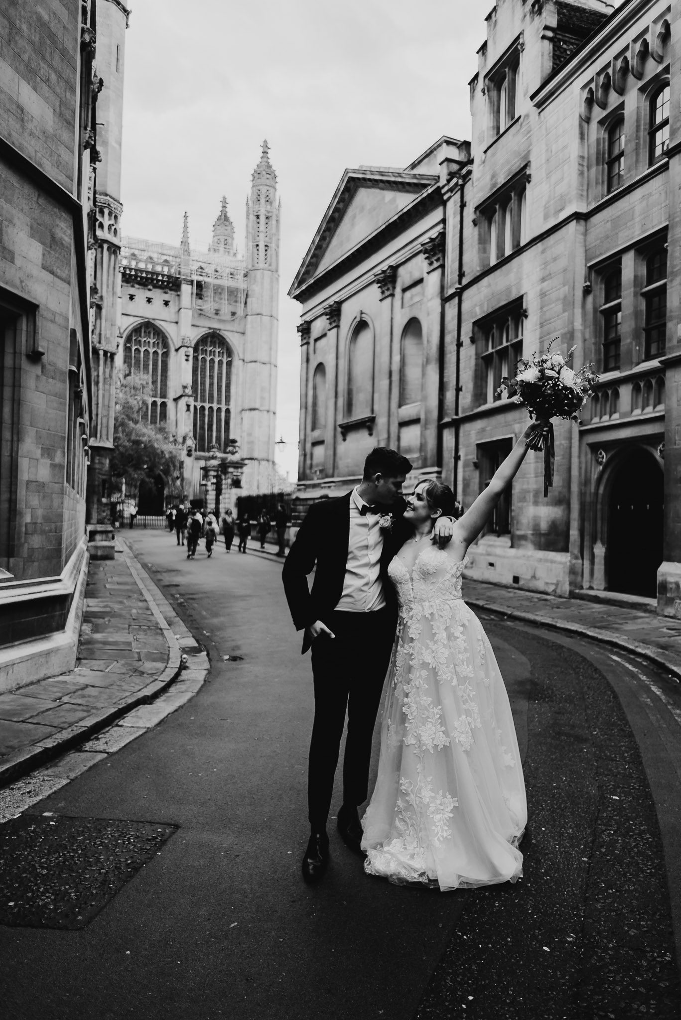 black and white image of bride and groom walking in the middle of Cambridge city and the bride is waving her flowers around