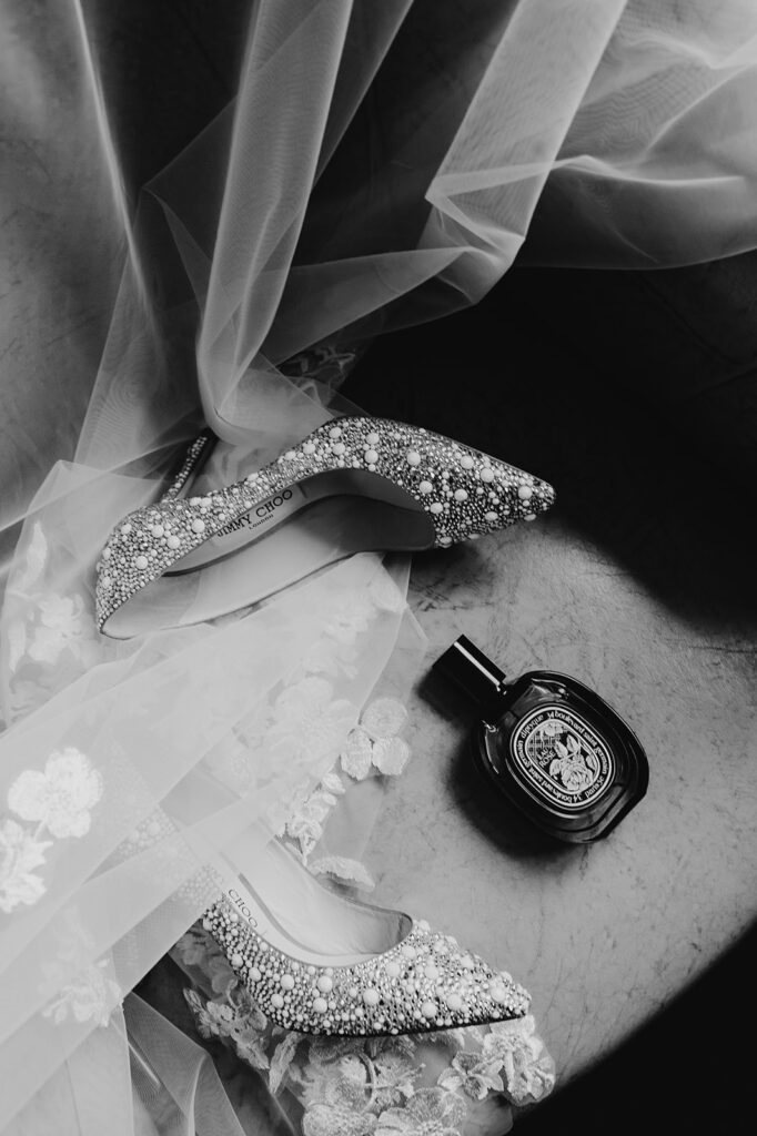 black and white image of bridal shoes, vail and perfume on a chair