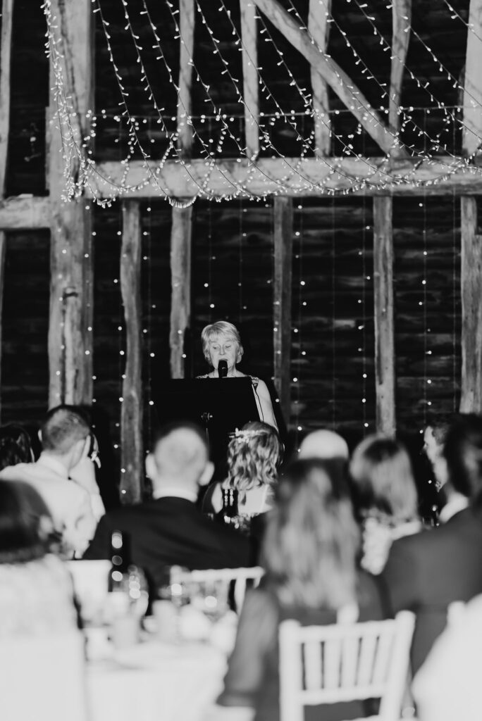 black and white image of the mother of the bride giving a speech to the wedding guests on stage