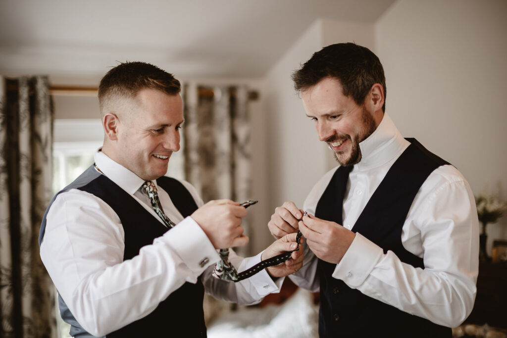 groomsmen and groom smiling and facing each other while holding a bowtie