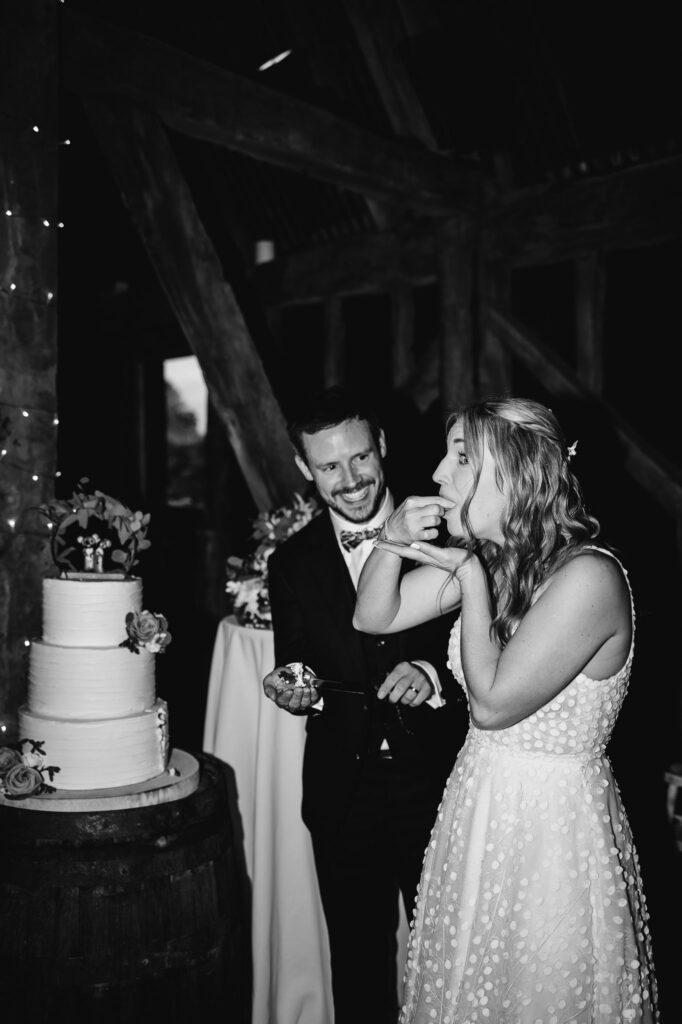 black and white image of bride eating wedding cake with the groom smiling and watching