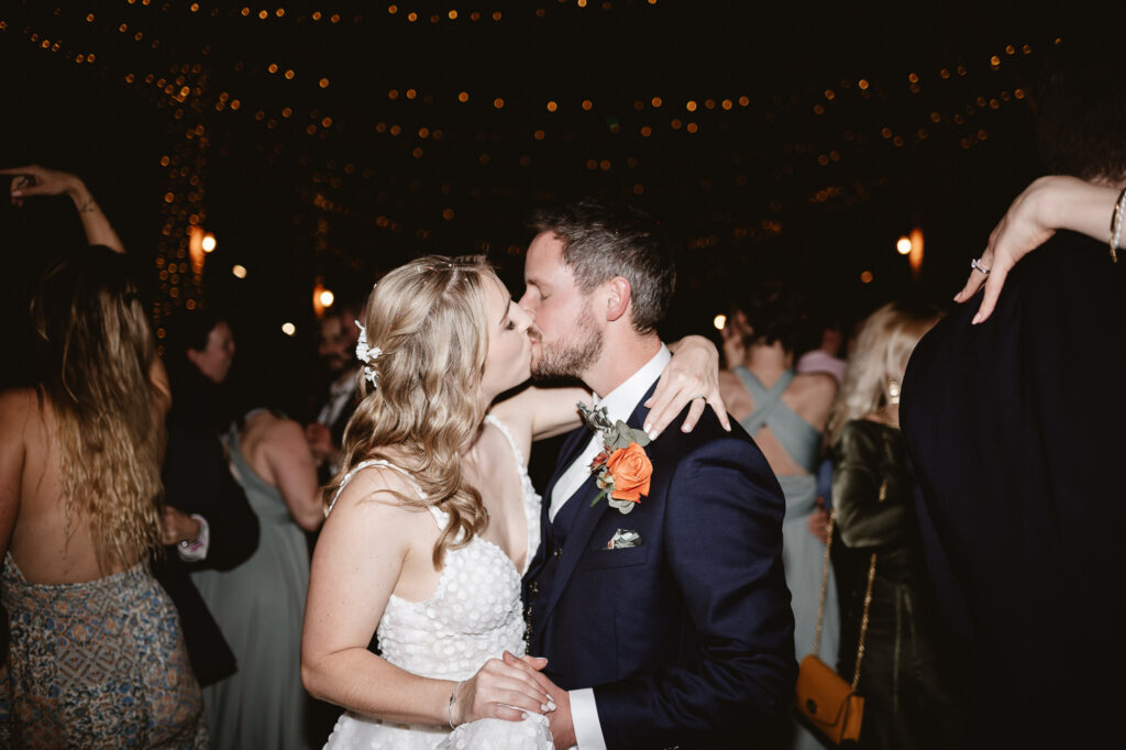 bride and groom kissing on the dance floor in the middle of guests dancing 