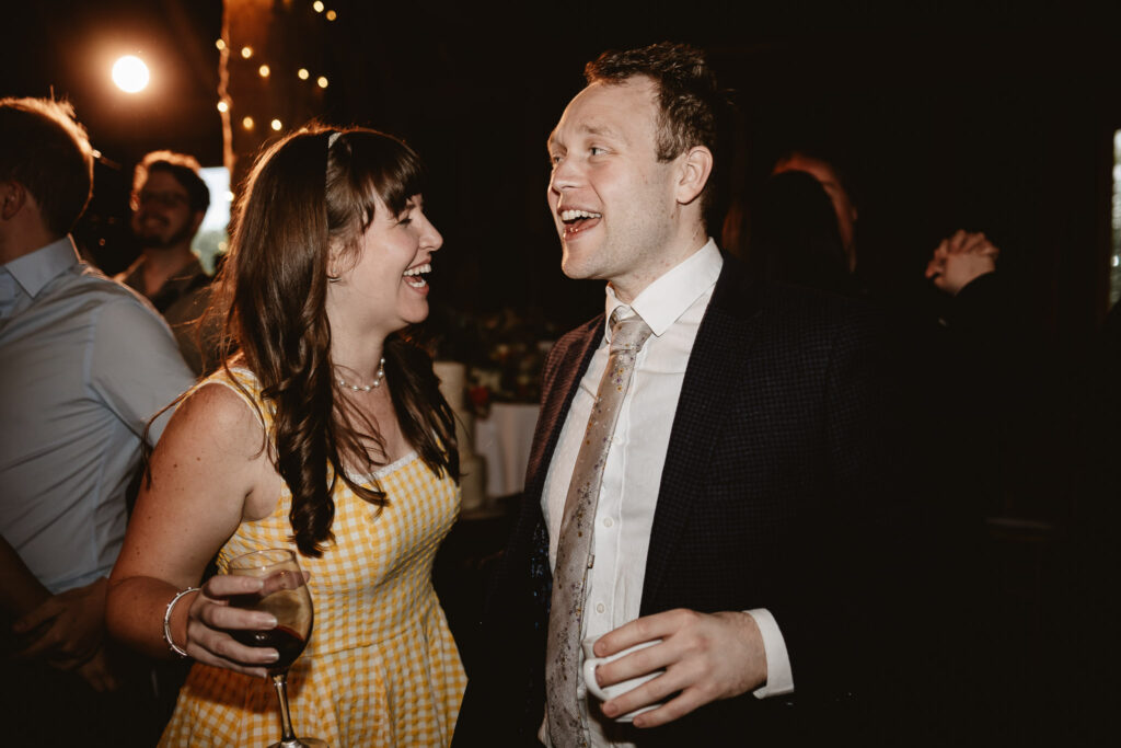 woman in yellow dress holding a drink while dancing and laughing with male in a suit on the dance floor