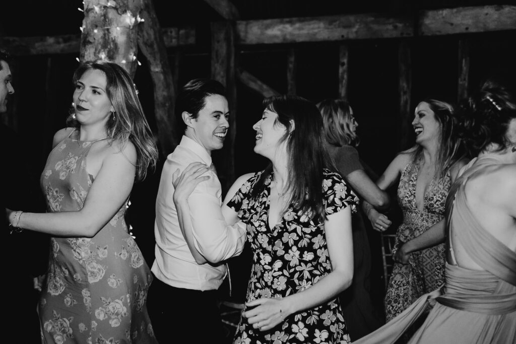 black and white image of wedding guests dancing and smiling on the dance floor 