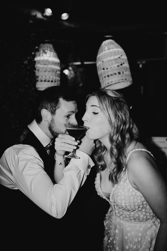 black and white image of bride and groom crossed arms and drinking cocktails