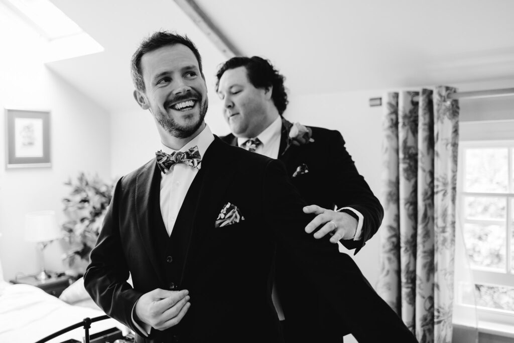 black and white image of the groom smiling while the groomsmen brushing hairs of his suit