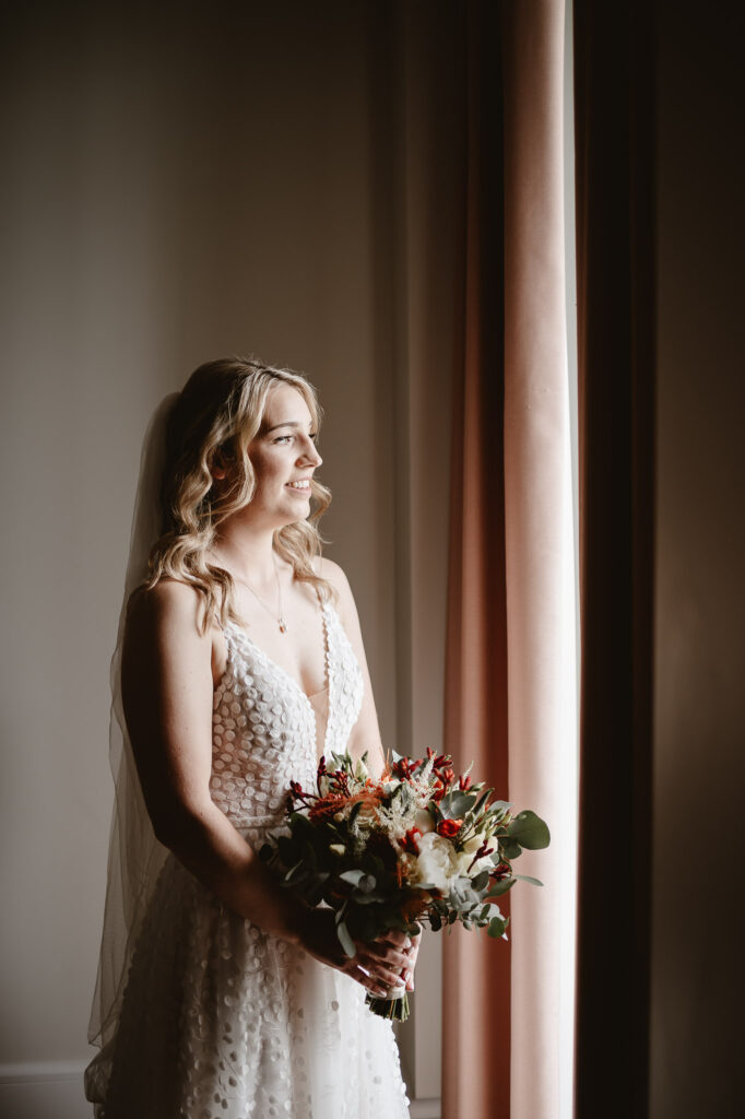 bride holding flowers looking out the window and smiling 