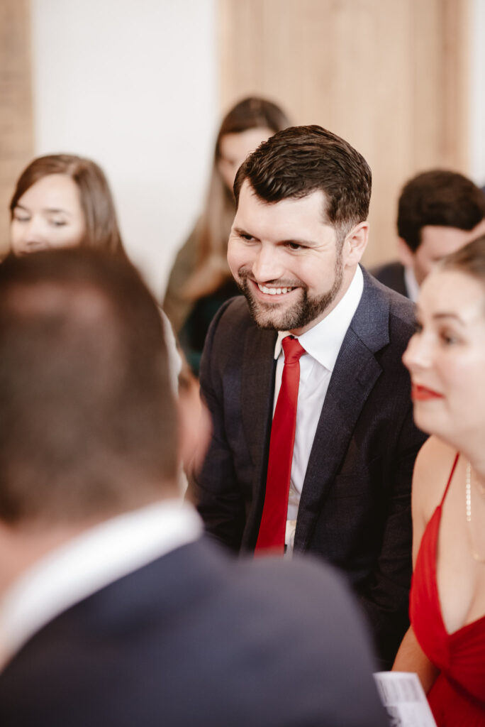 wedding guest dressed in a dark suit and red tie smiling with friends