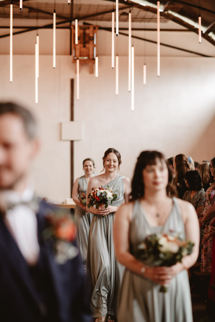 bridesmaids walking down the aisle wearing green dressed and holding flowers