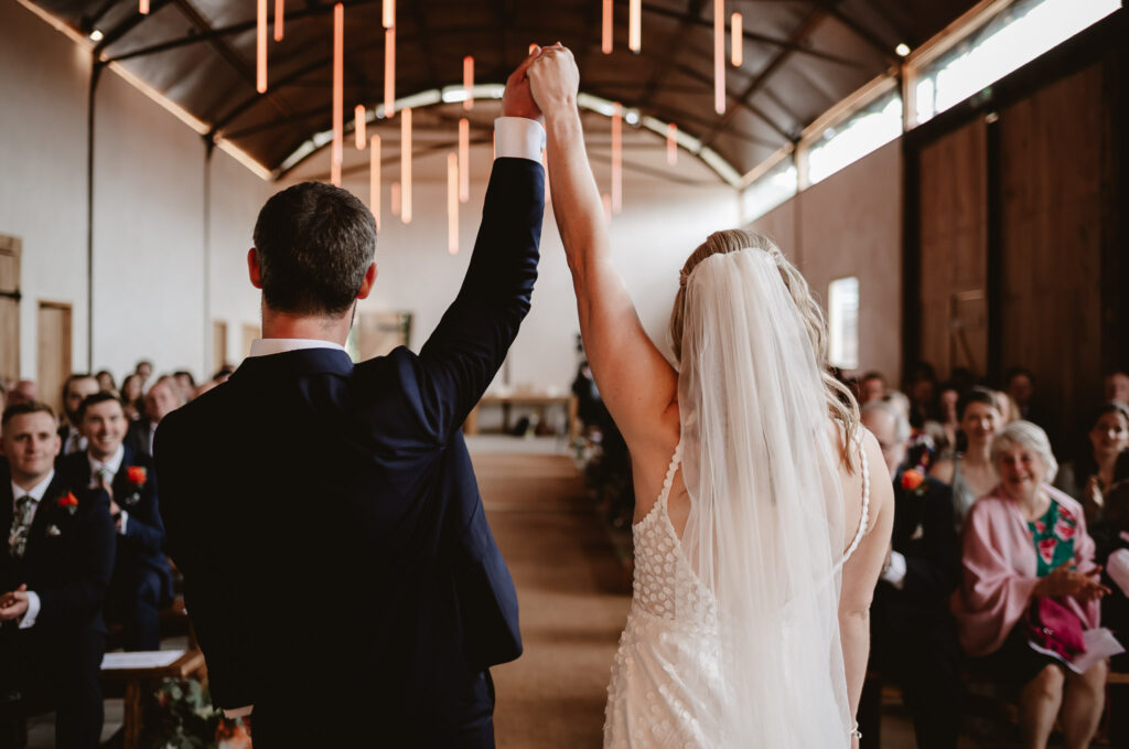 bride and groom holding hands high after the wedding ceremony in front of their guests