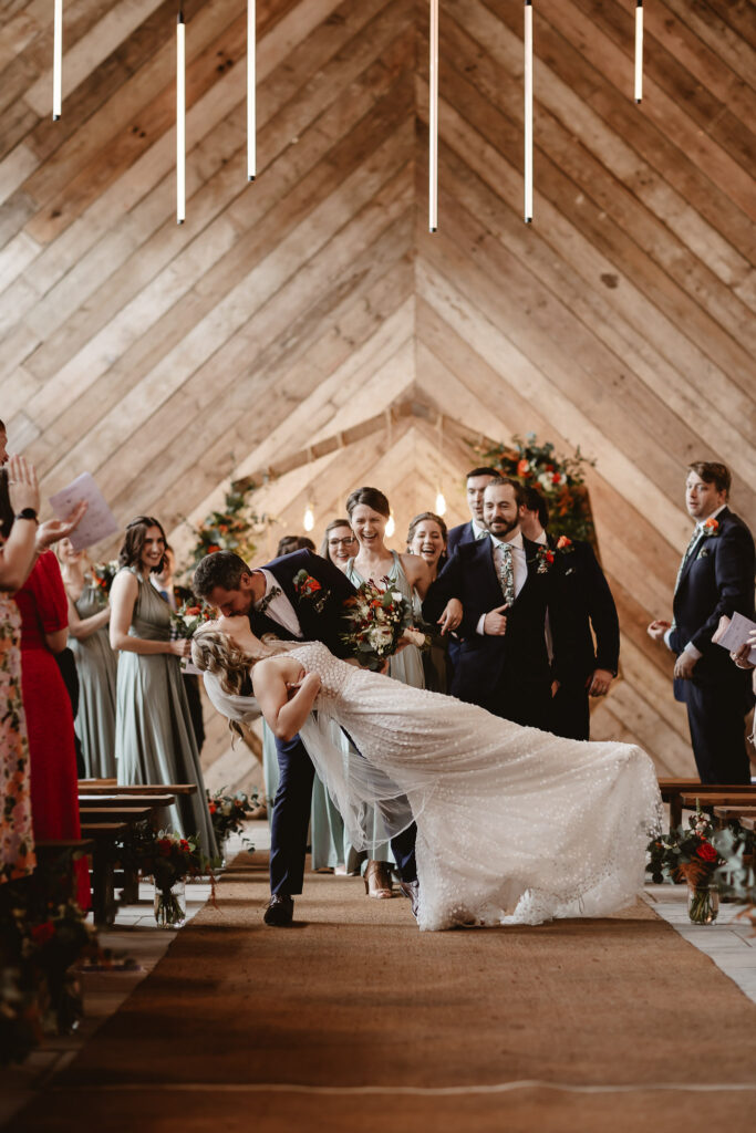 bride leans back on the groom and the couple kiss in front of their wedding guests 