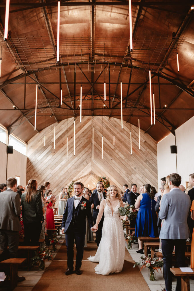 bride and groom holding hands and smiling walking down the aisle after the ceremony and past their wedding guests