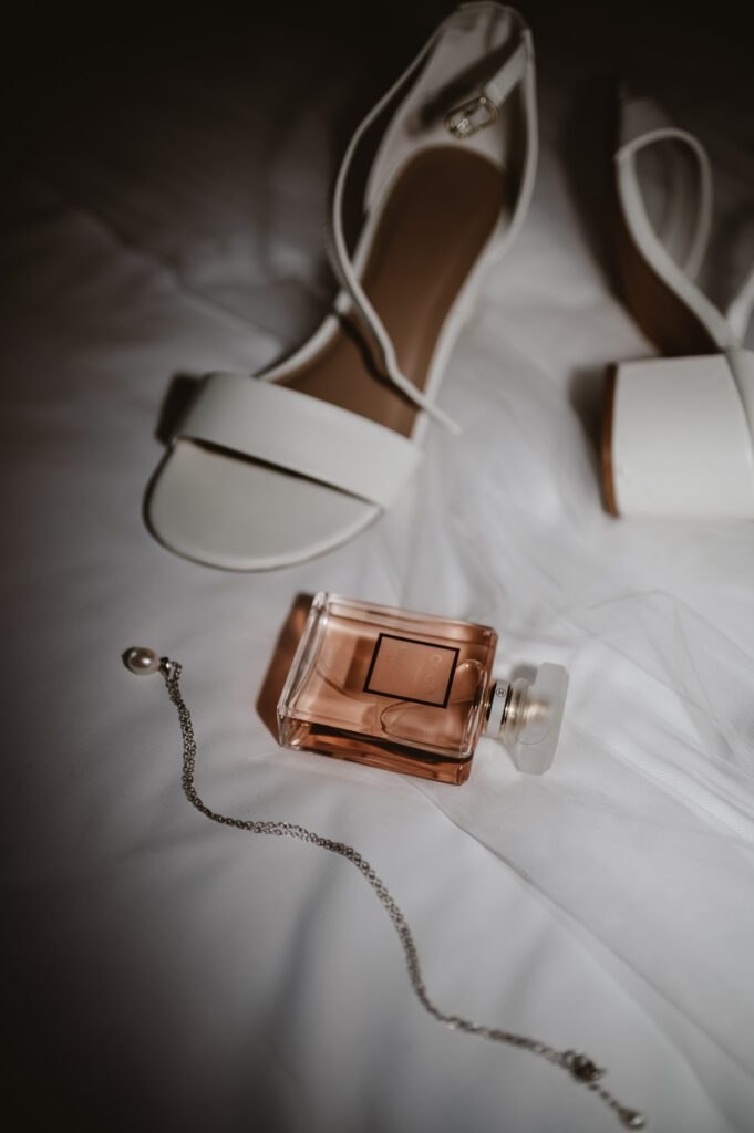 wedding details, wedding heels, coco chanel perfume and pearl necklace with the vail on a white bed