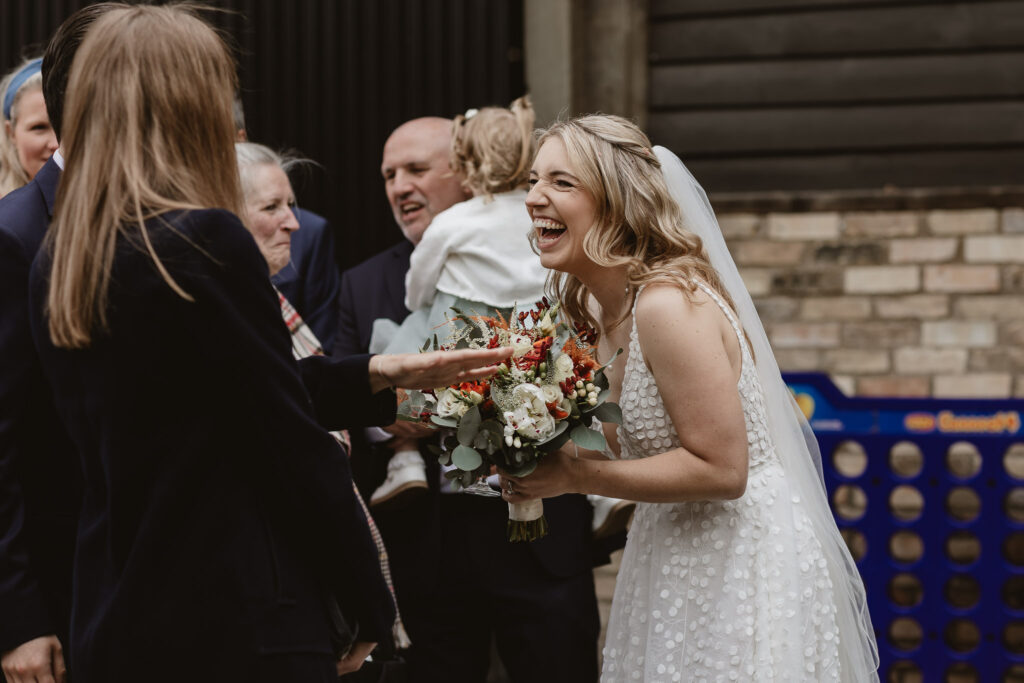 bride holding flowers and laughing with guests outside