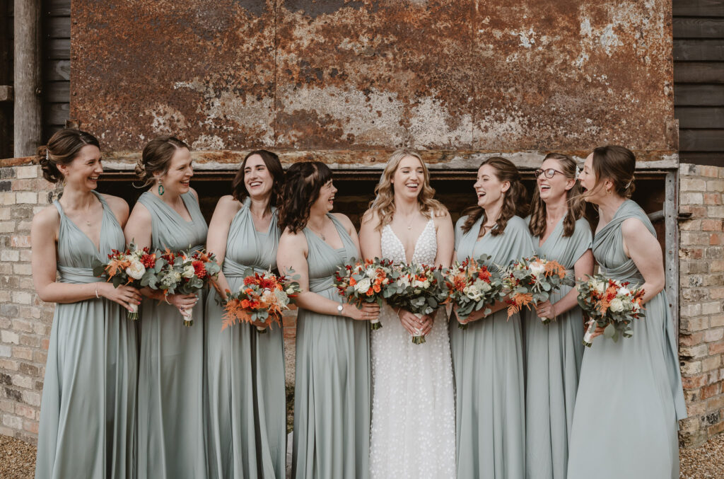 bridesmaids and bride holding flowers and laughing with each other