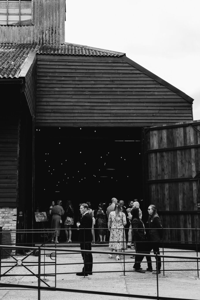 black and white image of barn and wedding guests socialising 