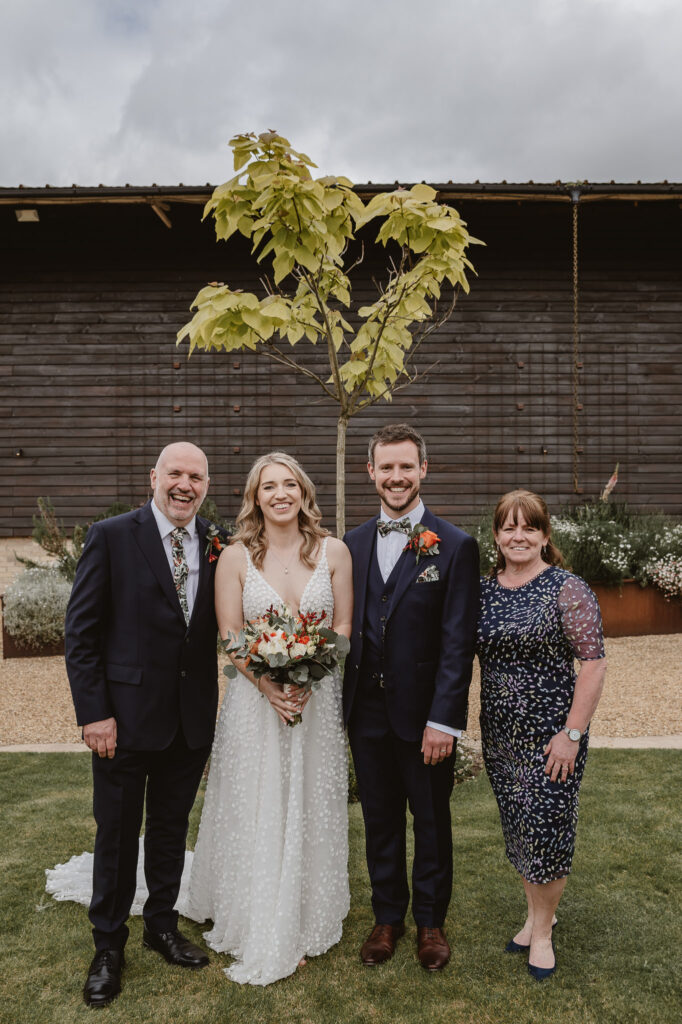 bride and groom standing with parents smiling for formal family photos in the gardens outside