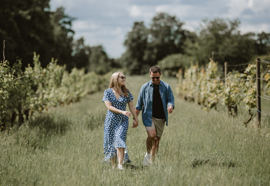 Couple holding hands and walking through vineyard smiling on a sunny day