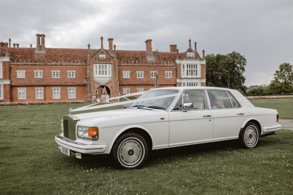 wedding vehicle rolls Royce in white driving on the grass outside the stately home at the wedding venue