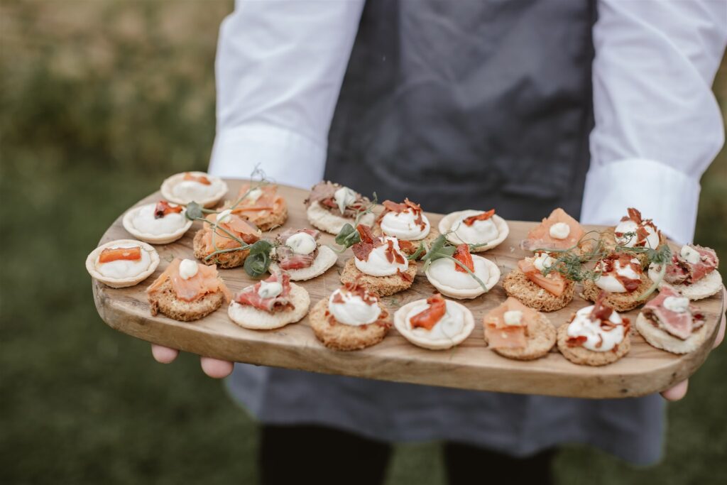 staff member at wedding venue serving canapes on a wooden board in the gardens outside