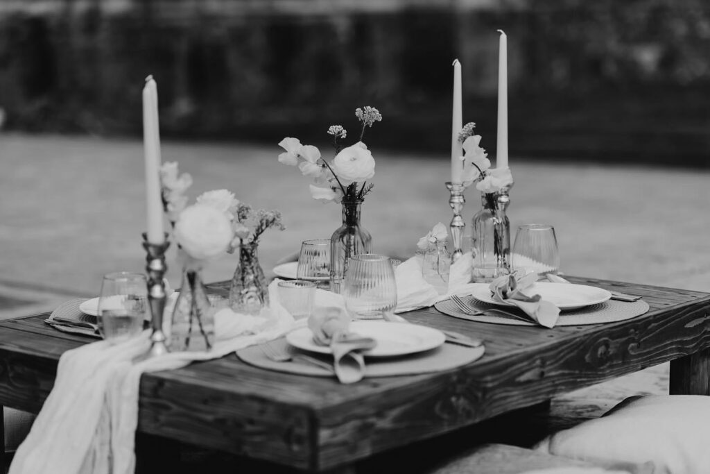 black and white image of a candle and flower in vases wooden table set up