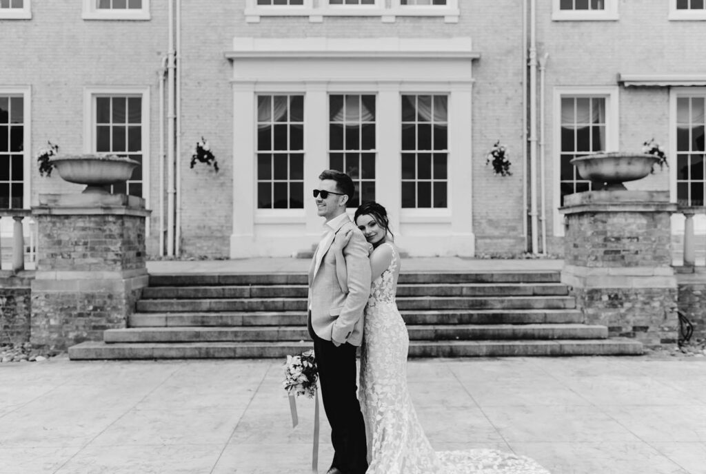 black and white image of bride hugging the grooms back outside the venue