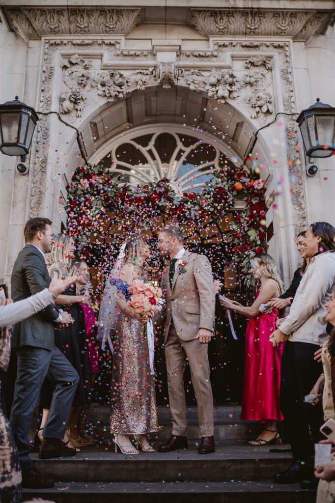 paper confetti being thrown in the air by wedding guests after the ceremony at the venue over the bride and groom 