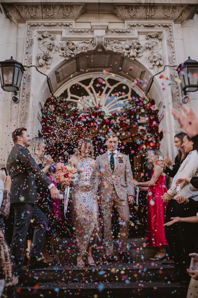 paper confetti being thrown in the air by wedding guests after the ceremony at the venue over the bride and groom 