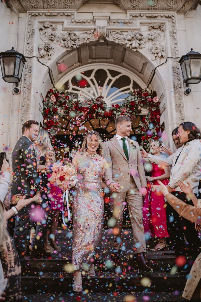 paper confetti being thrown in the air by wedding guests after the ceremony at the venue over the bride and groom 