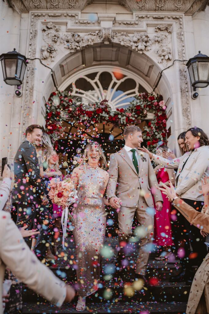 paper confetti being thrown in the air by wedding guests after the ceremony at the venue over the bride and groom 