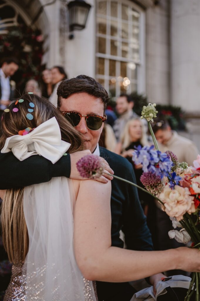 guest wearing sun glasses hugs bride with confetti in her hair