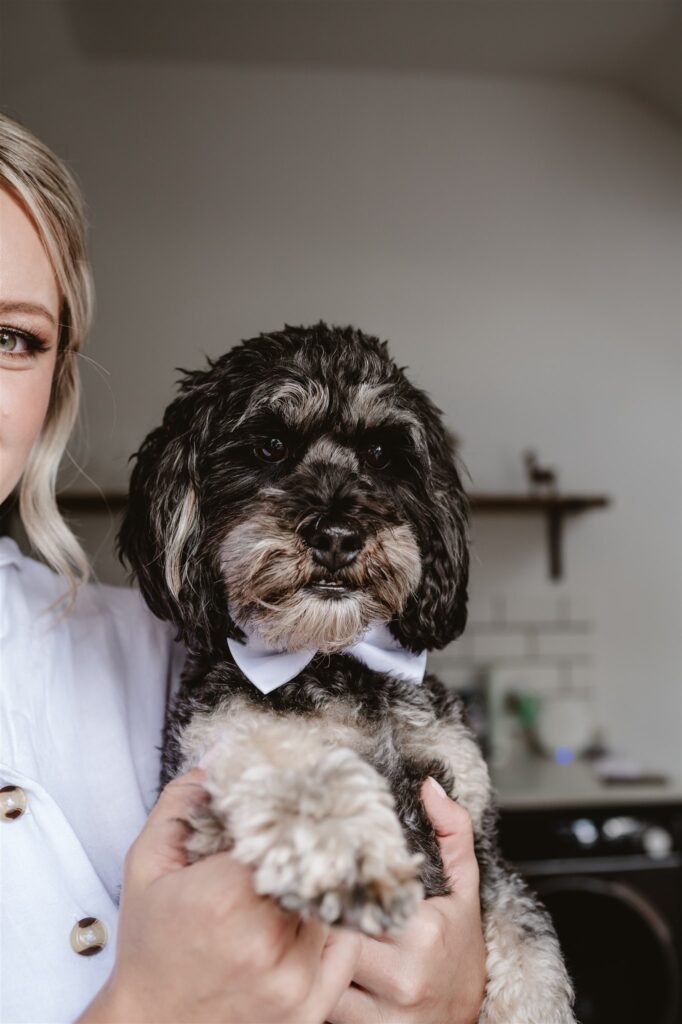 bride and bridesmaid in their pjs holding their dogs that are wearing a bow ties standing in the doorway during bridal prep at the wedding venue