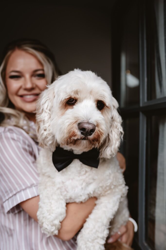 bride and bridesmaid in their pjs holding their dogs that are wearing a bow ties standing in the doorway during bridal prep at the wedding venue