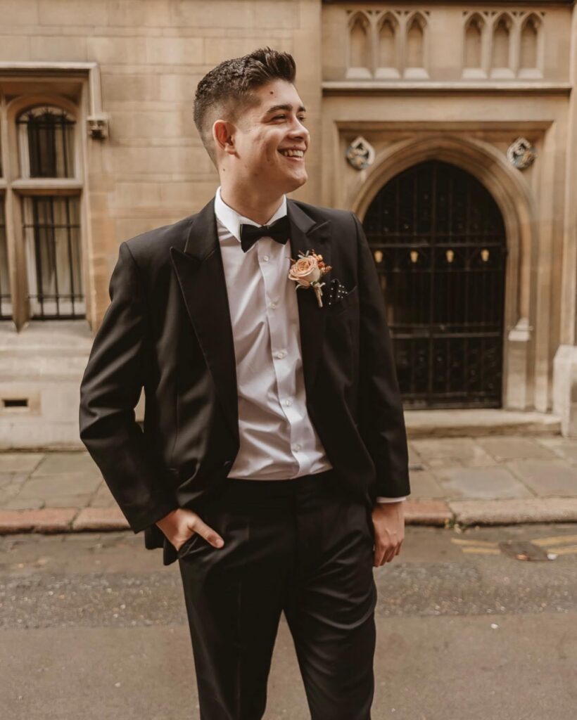 Groom smiling with hand in pocket wearing a bow tie suit in the middle of Cambridge city